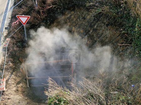 repairing pipes with hot water or steam in deep armored pit resembles a mine from which mist or dust is rolling. bounded by a temporary building fence as protection against the entry , tape barrier