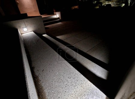 Foto de Iluminación de escaleras y escalones en la pared de hormigón al lado de las escaleras. reflectores empotrados brillan bajo los pies y crean una escena clara y segura para el movimiento por la noche. exterior del hotel del complejo - Imagen libre de derechos