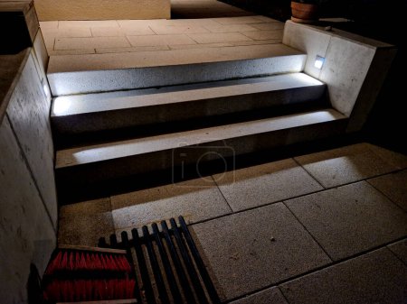 Foto de Iluminación de escaleras y escalones en la pared de hormigón al lado de las escaleras. reflectores empotrados brillan bajo los pies y crean una escena clara y segura para el movimiento por la noche. exterior del hotel del complejo - Imagen libre de derechos