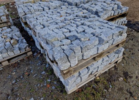 laying granite and marble light, white gray, medium size cubes. tilers put cobblestones in sand or gravel. they have piles ready to lay or wooden pallets occupy the passage on the sidewalk, quarry
