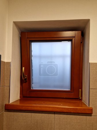 Das Toilettenfenster wird benutzt, um den Geruch zu belüften. hölzerner brauner Rahmen und ein Aufkleber auf dem Glas mit Unschärfeeffekt.
