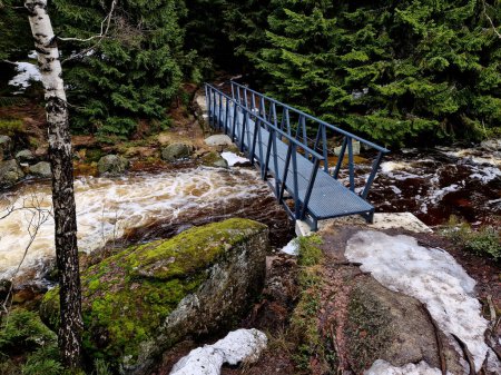 elementos furiosos de agua en un río de montaña. el mástil de madera dañado y derribado fue arrastrado por la inundación y aplastado contra las rocas. el nuevo puente duradero de metal resiste las olas de la