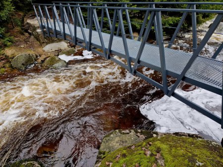 raging elements of water in a mountain river. the damaged and torn down wooden mast was washed away by the flood and crushed against the rocks. the new metal durable bridge withstands the waves of the