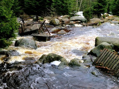 elementos furiosos de agua en un río de montaña. el mástil de madera dañado y derribado fue arrastrado por la inundación y aplastado contra las rocas. el nuevo puente duradero de metal resiste las olas de la