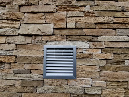 el conducto de ventilación con listones metálicos está sobre el revestimiento de piedra de la pared de una casa familiar o un edificio industrial. ventilación de gases de escape en el garaje de la casa