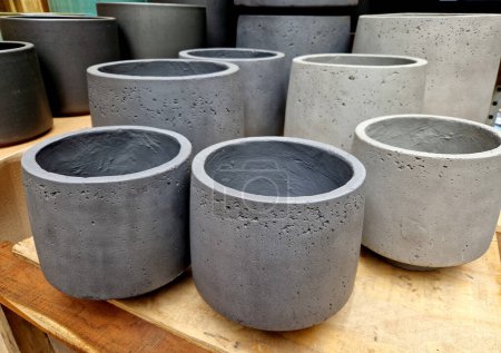 gray concrete flower pots, lined up in a warehouse in rows for sale. plastic white tubs of bricks stacked on top of each other. production of cheap design containers for plant, table