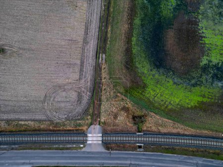 railway track is across a field wet and green with algae. there is a crossing and a road next to train track. height view. safety of drivers is on attention and respect collision with train