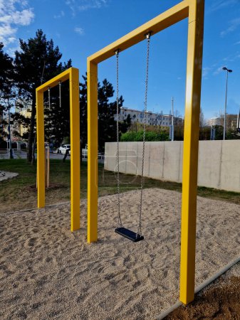 Massive wood beams in the shape of a square gate or frame, between which is a metal rod on which are swings for children. lawn by the park path. roof, metal sheet, aerial, view  footpath, lawn