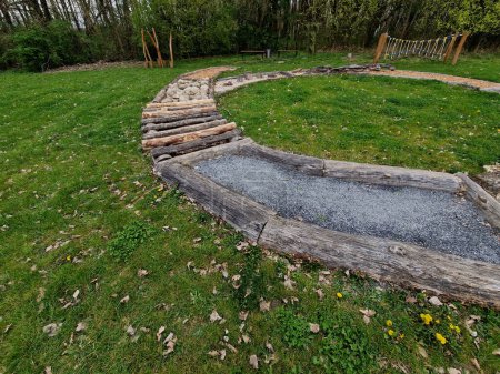 Tactile path for bare feet awakens the senses and uneven endings on the feet alternating different materials wood stone gravel sand bark in a park environment, sensoric, red, bent, curved, log