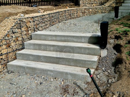 Photo for Concrete stairs to the park serving at the same time as a sitting bench. gray cement clean smooth bright cement surface. granite cubes paving threshing gravel road. overgrown with plants. anti-slip - Royalty Free Image