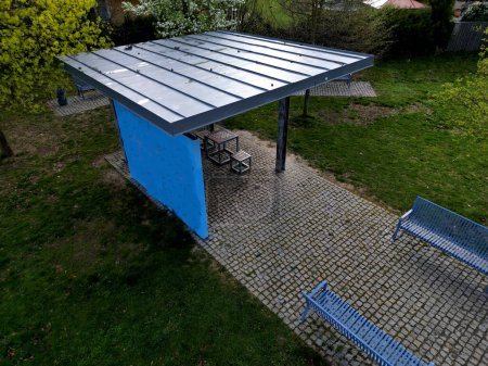 pergola of metal galvanized construction with blue planks in the side. under the shades there is a bench. city shelter for lectures and concerts. public gazebo modern look