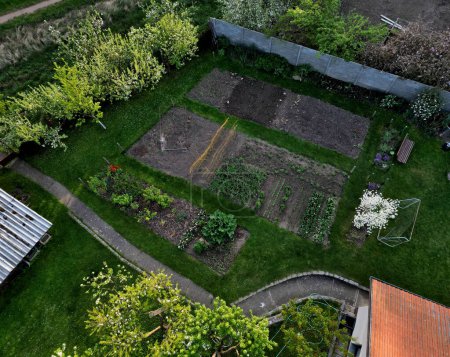 Téléchargez les photos : Porte-vêtements dans le jardin avec potager et objectifs de football. les buissons à fleurs printanières et les champs et le toit - en image libre de droit