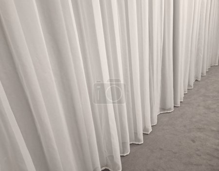 Foto de La cortina cuelga del techo al suelo. suave cortina sintética satinada que divide el espacio y forma un fondo textil suave. pesos en la parte inferior del borde de la tela - Imagen libre de derechos