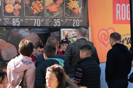 Téléchargez les photos : Chisinau, Moldavie - 15 octobre 2022 : Des hommes et des femmes se tiennent à un comptoir mobile avec de la restauration rapide lors de la célébration de la Journée de la ville, Chisinau. Chisinau est la capitale de la Moldavie. Concentration sélective. - en image libre de droit