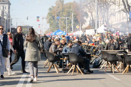 Téléchargez les photos : Chisinau, Moldavie - 15 octobre 2022 : Les gens marchent le long de l'avenue Stefan cel Mare, mangent de la nourriture de rue, se détendent le jour de la fête de la ville. Au-dessus du peuple se trouve la fumée d'une cuisine extérieure. Concentration sélective. - en image libre de droit