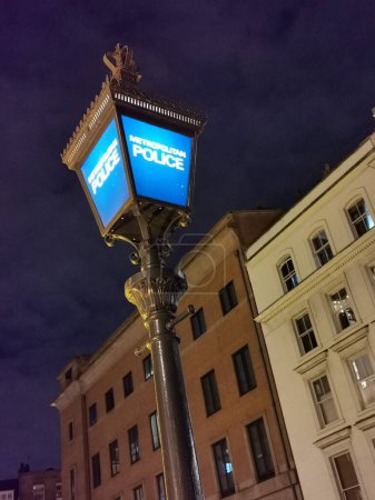 Téléchargez les photos : Ancien réverbère de la police allumé la nuit, Londres, Angleterre, Royaume-Uni montré au crépuscule avec ciel bleu profond - en image libre de droit