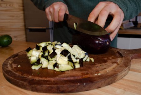 Foto de Cortar berenjenas con un cuchillo y una tabla de madera en la cocina - Imagen libre de derechos