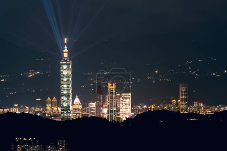 Foto de The light from the blue lasers on top of the tower shines in all directions. Night view of the city surrounded by mountains is hazy and dreamy.. Taipei City, Taiwan - Imagen libre de derechos