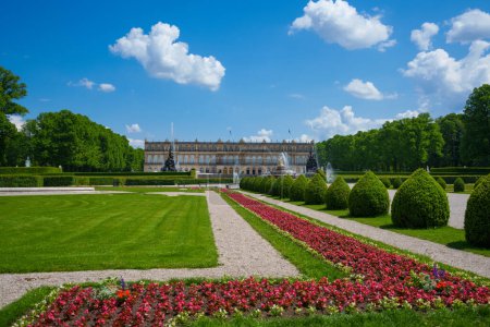 Summer garden landscape. Blue sky and white clouds, trees, grass, red flowers. Schloss Herrenchiemsee is located on the castle island of Chiemsee, Germany.