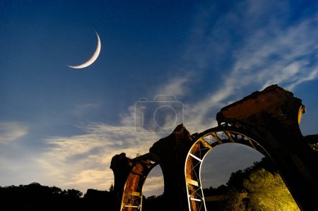 Foto de La luna creciente en una noche de otoño parece discreta y discreta. Longteng Broken Bridge es una atracción histórica junto a la carretera en las colinas. - Imagen libre de derechos
