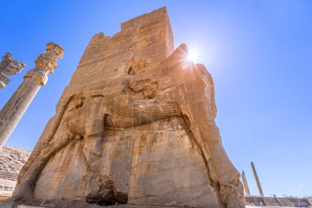 Imposing Lamassu statues stand tall, casting intricate shadows amidst the ancient ruins of Persepolis, Iran. Captured on a bright day with the blue sky and clouds.