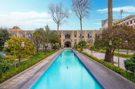 Téléchargez les photos : Hôtel Abbasi, Ispahan, Iran - 4 mars 2024 : Jardins persans tranquilles avec une voie navigable centrale menant à la façade historique. Verdure luxuriante et arbres rehaussent la vue. - en image libre de droit