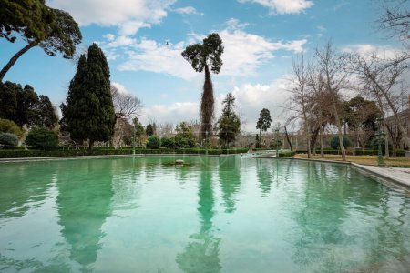 Les piscines sereines du palais du Golestan se reflètent par des arbres imposants contre un ciel nuageux. Site historique, Téhéran, Iran.