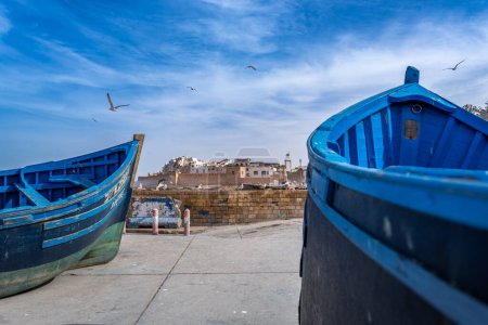 Vivid blue boats sit on land and seagulls fly above the Moroccan city of Essaouira, capturing the essence of this coastal city.