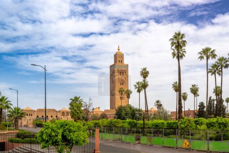 The iconic minaret of the Koutoubia Mosque towers under the blue sky and is surrounded by lush palm trees. A testament to the rich cultural heritage of Marrakech, Morocco.