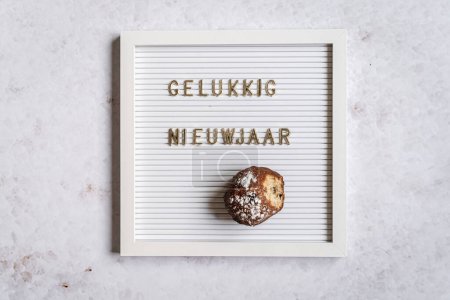 Téléchargez les photos : A white letterboard with the text in golden letters spelliing Gelukkig Nieuwjaar (Dutch for Happy New Year) with one oliebol - en image libre de droit