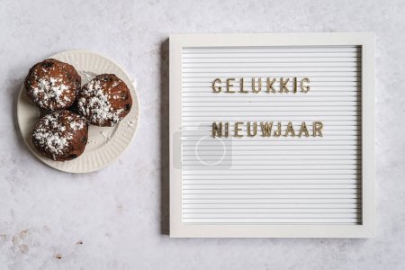 Téléchargez les photos : A white letterboard with the text in golden letters spelliing Gelukkig Nieuwjaar (Dutch for Happy New Year) with oliebollen next to it - en image libre de droit
