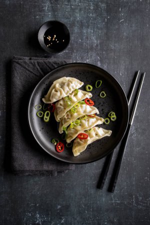 Foto de Un plato con dumpling gyoza fresco sobre plato negro y fondo con palillos y servilleta - Imagen libre de derechos