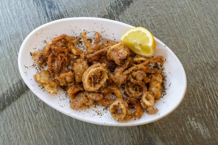 Photo for A plate of fried squid or calamari with lemon on a white plate, horizontal - Royalty Free Image