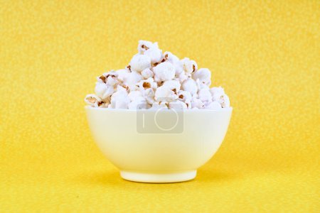 Foto de Un tazón blanco de palomitas de maíz saladas sobre un fondo amarillo con espacio para la publicidad. vista de cerca - Imagen libre de derechos