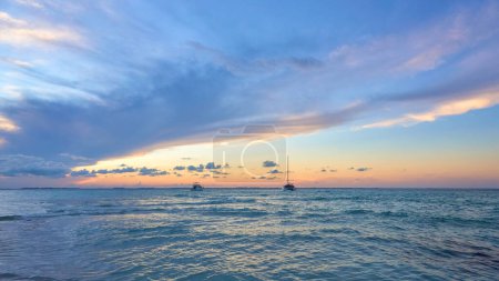 2 yachts at sunset on north beach isla mujeres. blue and orange tones in the sky full of clouds. mexican caribbean beaches. landscape photography.