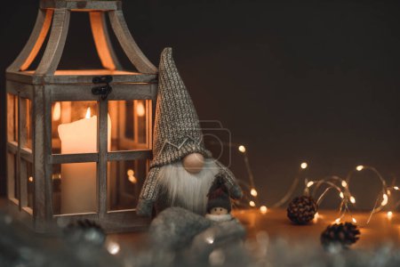 Photo for A cute dwarf in a high hat and a snowman on a brown background, decorated with lanterns with a candle, cones and a garland. Suitable for postcards and Christmas greetings - Royalty Free Image