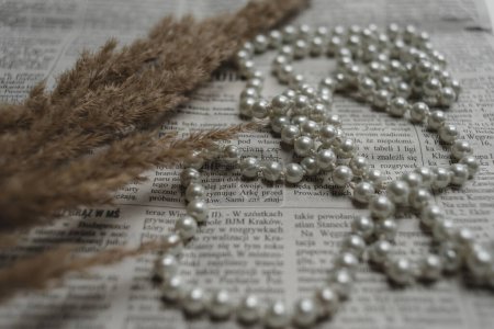 Téléchargez les photos : Une série de perles et de pierres précieuses se trouvent sur un journal, une photo dans un style rétro élégant. - en image libre de droit