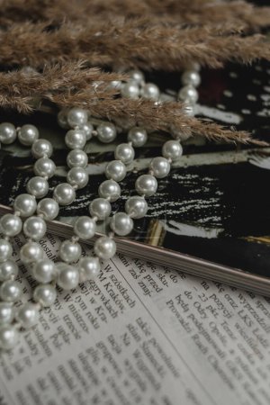 Téléchargez les photos : Une chaîne de perles, un magazine et des fleurs séchées reposent sur un journal, une photo dans un style rétro élégant. - en image libre de droit
