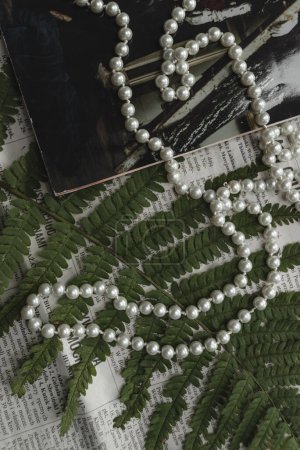 Téléchargez les photos : Une chaîne de perles repose sur le fond d'une feuille de fougère verte, d'un magazine et d'un journal.. - en image libre de droit