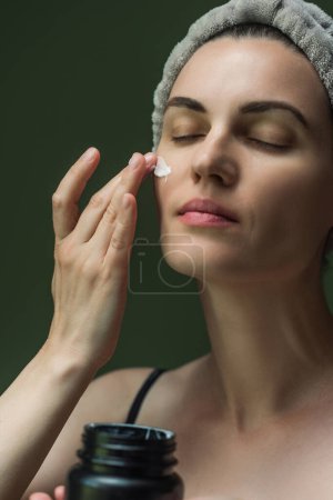 Photo for An attractive European woman puts cream on her face. Close-up of the beauty industry, cosmetology. Skin care at home - Royalty Free Image