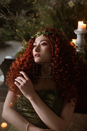 Foto de Hada mujer de pelo rojo con velas, flores y plantas, princesa druida fantasía oscura - Imagen libre de derechos