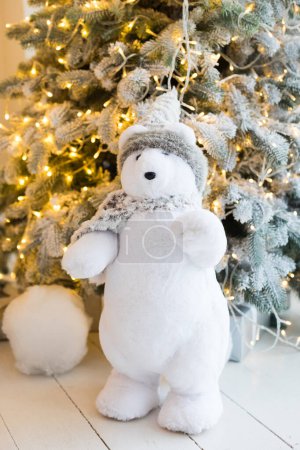 Téléchargez les photos : Arbre de Noël avec neige artificielle et guirlandes, un ours en peluche blanc, des boîtes avec des cadeaux du Nouvel An, sol en bois - en image libre de droit