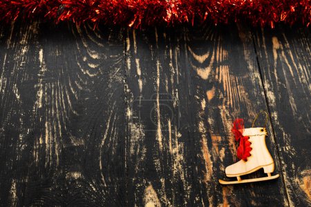 Photo for Christmas flat lay with place for text, red tinsel and wooden skates lying on a dark wooden table - Royalty Free Image