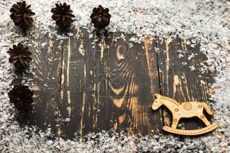 Foto de Navidad plana con lugar para texto, nieve artificial, juguete de caballo de madera y conos se encuentran en una mesa de madera oscura - Imagen libre de derechos