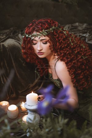 Téléchargez les photos : Fée rousse femme aux cheveux avec des bougies, des fleurs et des plantes, sombre fantaisie druide princesse - en image libre de droit
