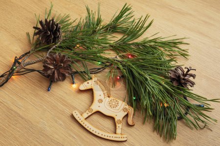 Foto de Juguete de caballo de Navidad de madera con adorno, rama de pino, conos y una guirnalda se encuentran sobre la mesa - Imagen libre de derechos