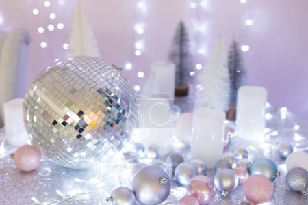 Photo for Disco ball, white, silver, pink and blue Christmas balls and a garland lie on a table with a tablecloth with sparkles,  bokeh - Royalty Free Image