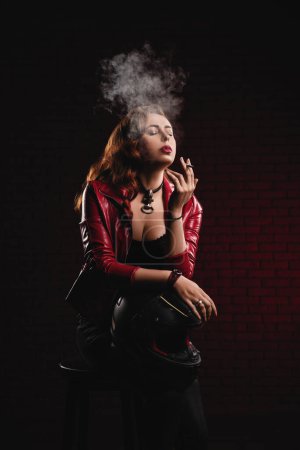 Foto de Bonita mujer con casco de motocicleta y cigarrillo sobre fondo de pared de ladrillo - Imagen libre de derechos