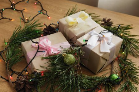 Téléchargez les photos : Cadeau de Noël en papier artisanal avec ruban jaune, branches de pin, cônes et guirlande sur la table en bois - en image libre de droit