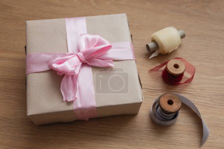 Téléchargez les photos : Cadeau d'anniversaire en papier artisanal, avec ruban rose et trois bobines avec rubans sur la table en bois - en image libre de droit